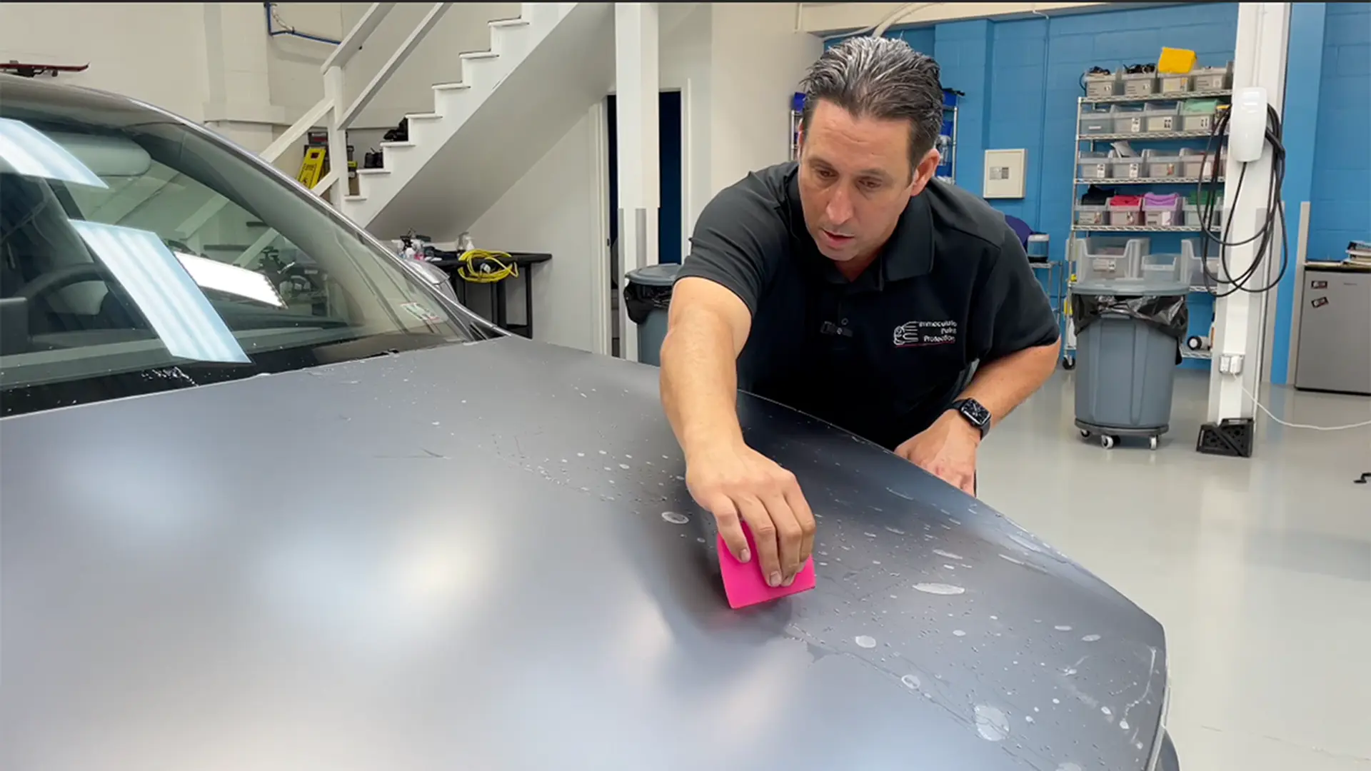 Bill Fetter actively installing SunTek matte paint protection film (PPF) on the hood of a 2026 Quicksilver Tesla Model Y. This "in-process" shot shows how we protect Tesla paint, with half the hood revealing the finished frosted stealth look and the other half showing the installation slip solution being worked out.