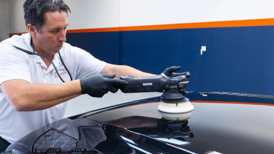 Close-up of Bill performing heavy compound paint correction on a Santorini Black 2024 Land Rover Defender. This intensive machine polishing stage levels the clear coat to remove deep scratches and wash swirls, creating the perfect flawless canvas required for a professional ceramic coating.
