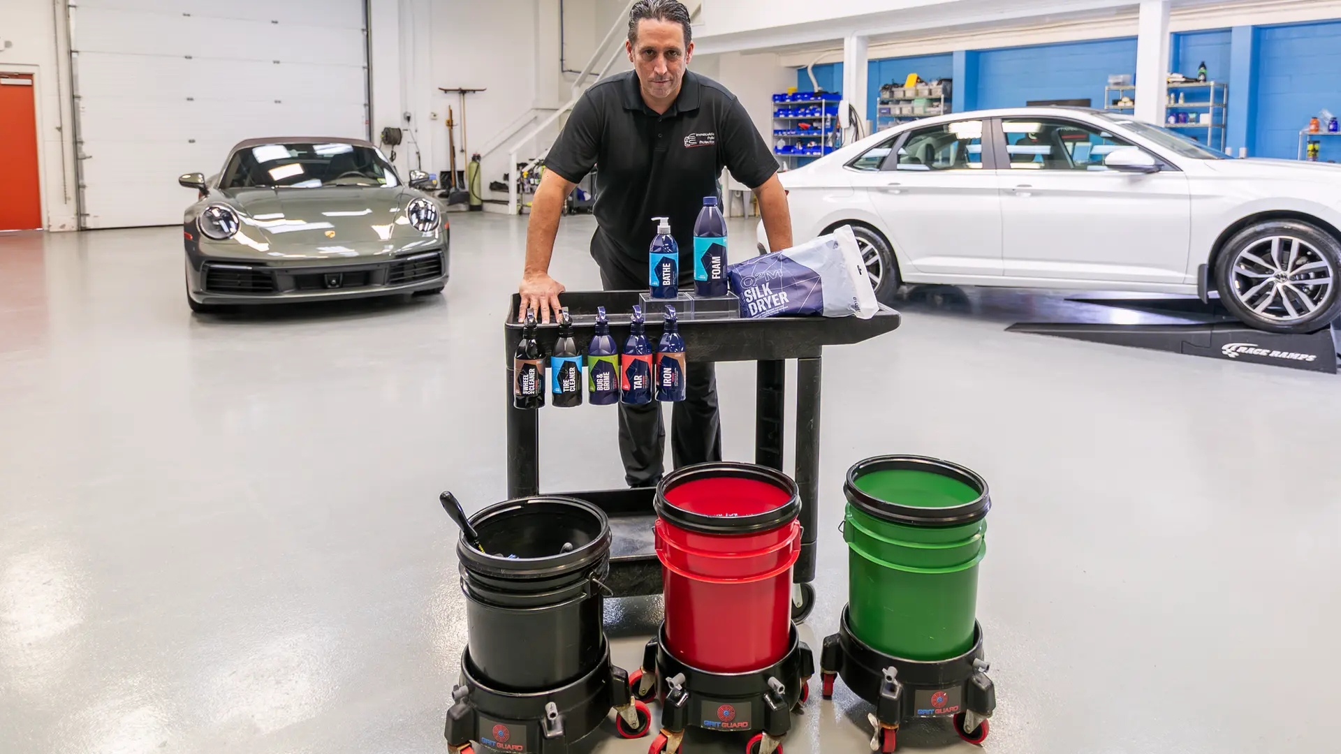 Having the right supplies is the first step in learning how to wash a car properly by hand. Here, Immaculate Paint Protection founder Bill Fetter stands behind a detailing cart loaded with his recommended professional-grade Gyeon products, including Gyeon Bathe, grit guards, and premium wash mitts. Bill recommends this exact setup to his clients as the best way to hand wash car exteriors safely at home, especially for maintaining ceramic coated and PPF-protected vehicles.