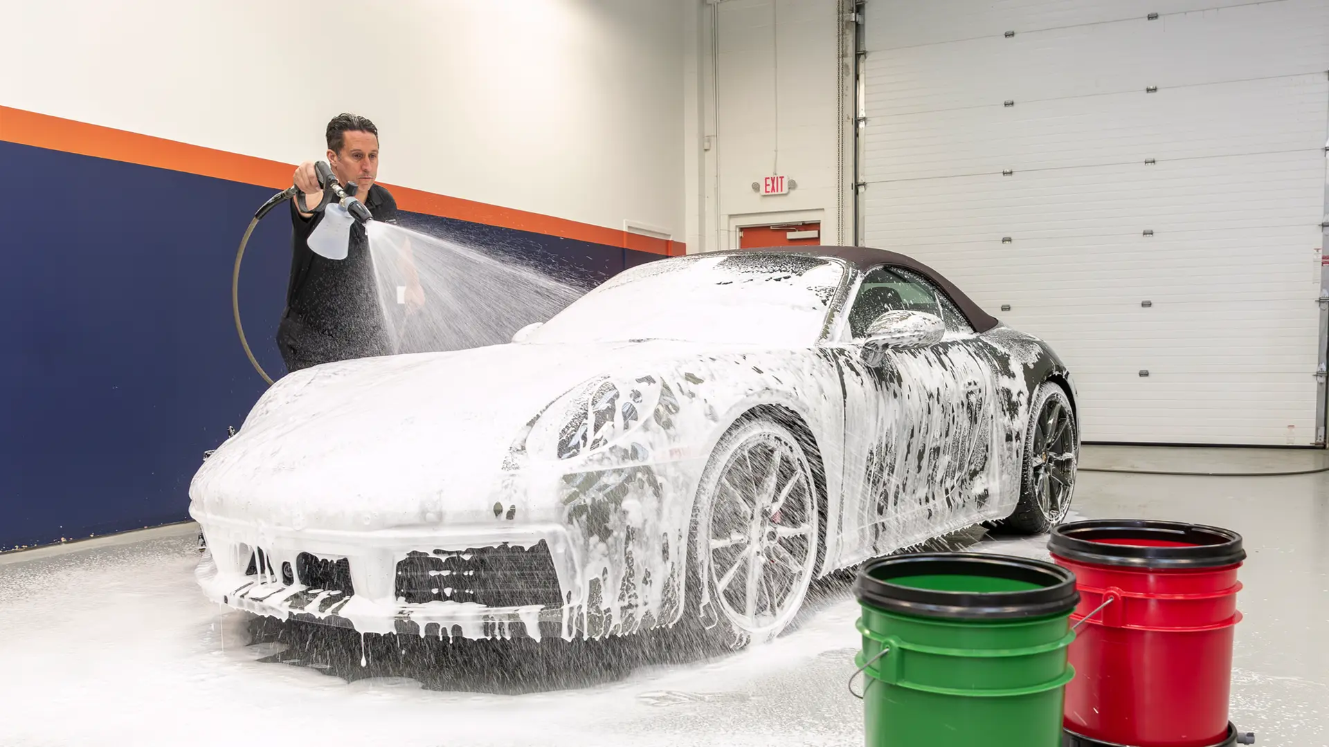 Learning how to hand wash a car properly starts before you even touch the paint. The best way to hand wash car exteriors safely is to begin with a thick foam pre-soak. Here, Bill from Immaculate Paint Protection is using a foam cannon to spray Gyeon foam on a 2020 Porsche 911 Convertible. This vital step loosens heavy grit and grime so it can be rinsed away, preventing scratches during the wash process.