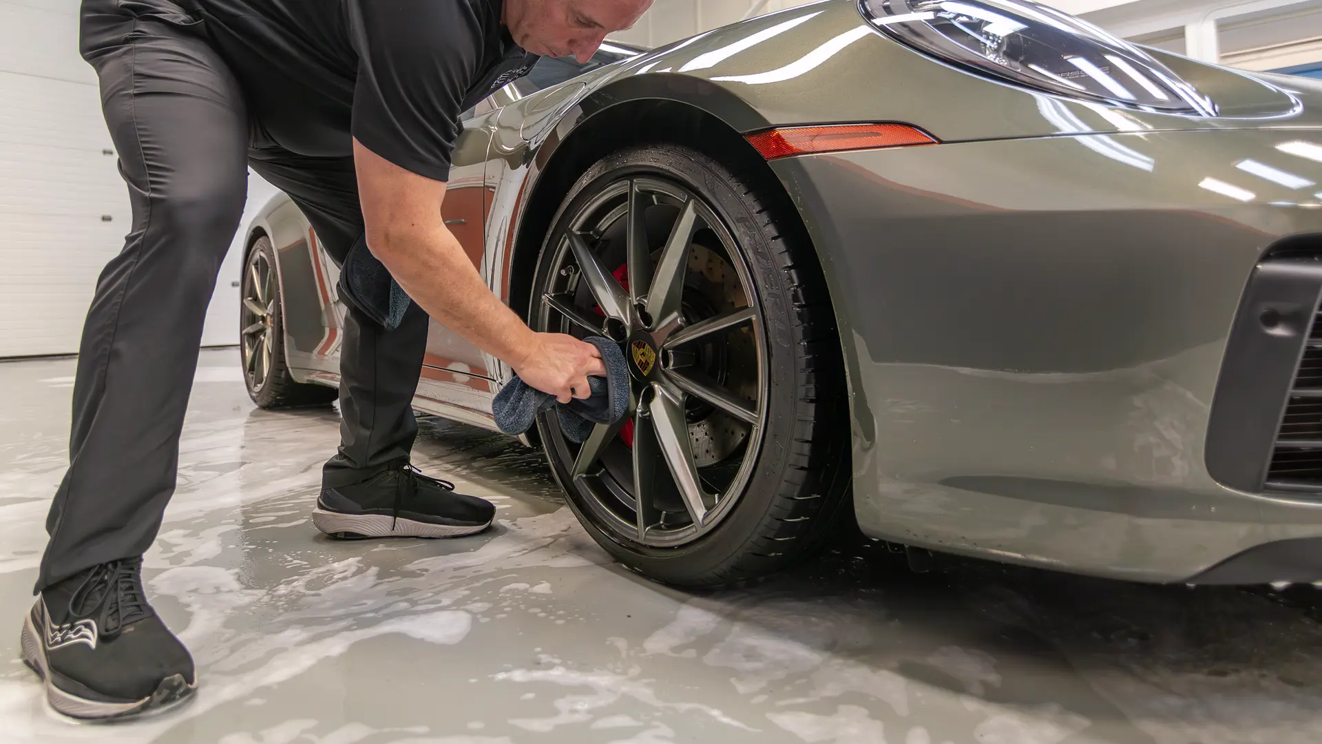 When learning how to hand wash a car safely, a critical mistake is using the same car wash towel on both the wheels and the paint. Here, Immaculate Paint Protection founder Bill Fetter demonstrates the correct method by using a dedicated black towel exclusively to dry the wheels of a 2020 Porsche 911 Convertible. This strict separation ensures that brake dust and tiny rocks picked up from the wheels never scratch the delicate body panels.