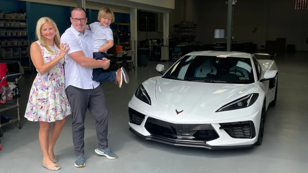 A happy local family consisting of a mom, dad, and young son smiling next to their newly protected white 2023 Chevrolet Corvette at the Immaculate Paint Protection shop in the Lehigh Valley.