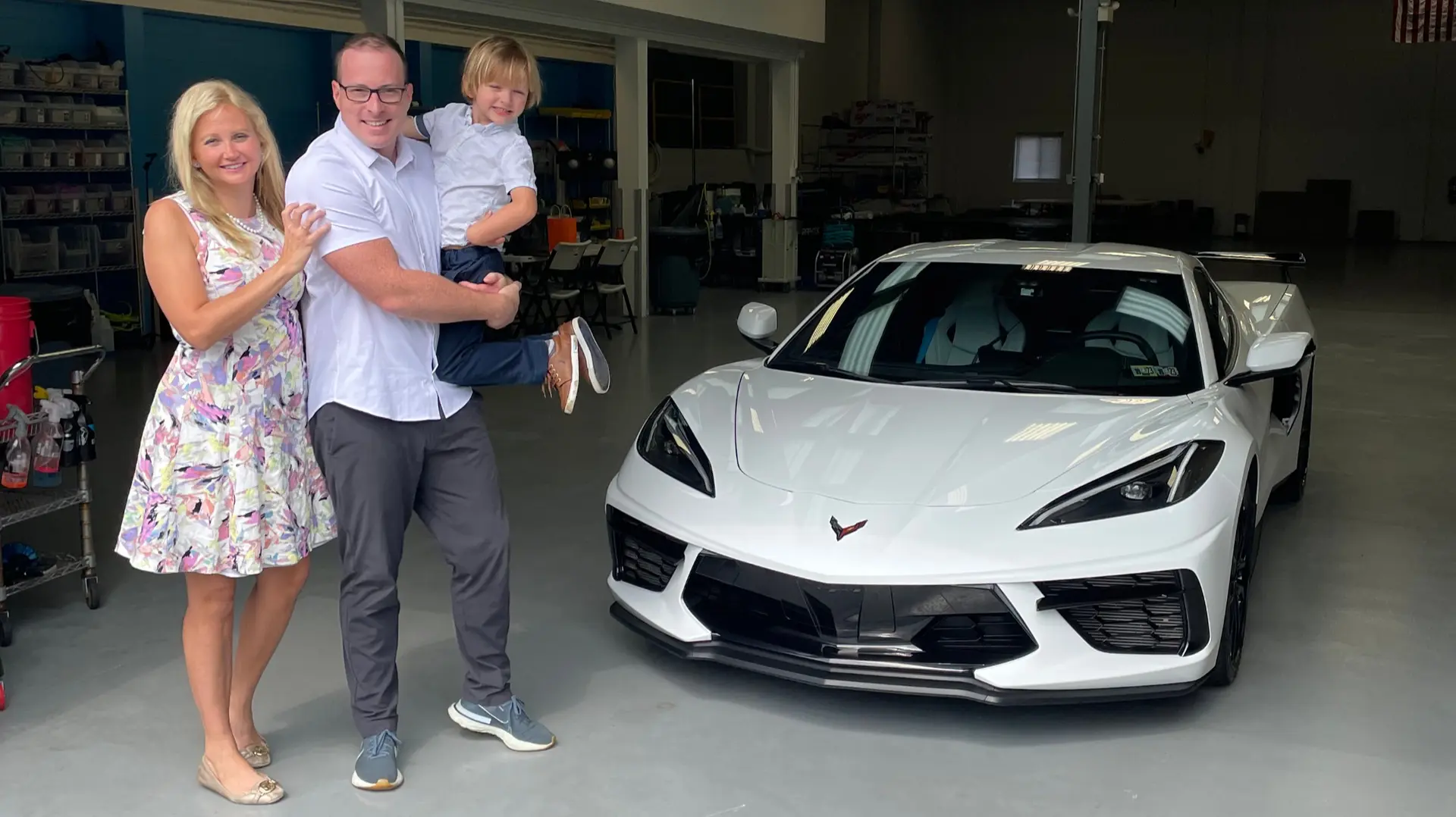 A happy local family consisting of a mom, dad, and young son smiling next to their newly protected white 2023 Chevrolet Corvette at the Immaculate Paint Protection shop in the Lehigh Valley.