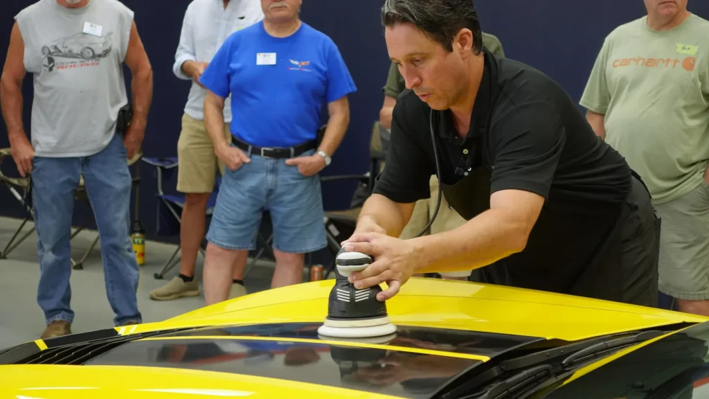 Bill Fetter machine polishing the hood of a yellow corvette in front of the Allentown Area Corvette Club.