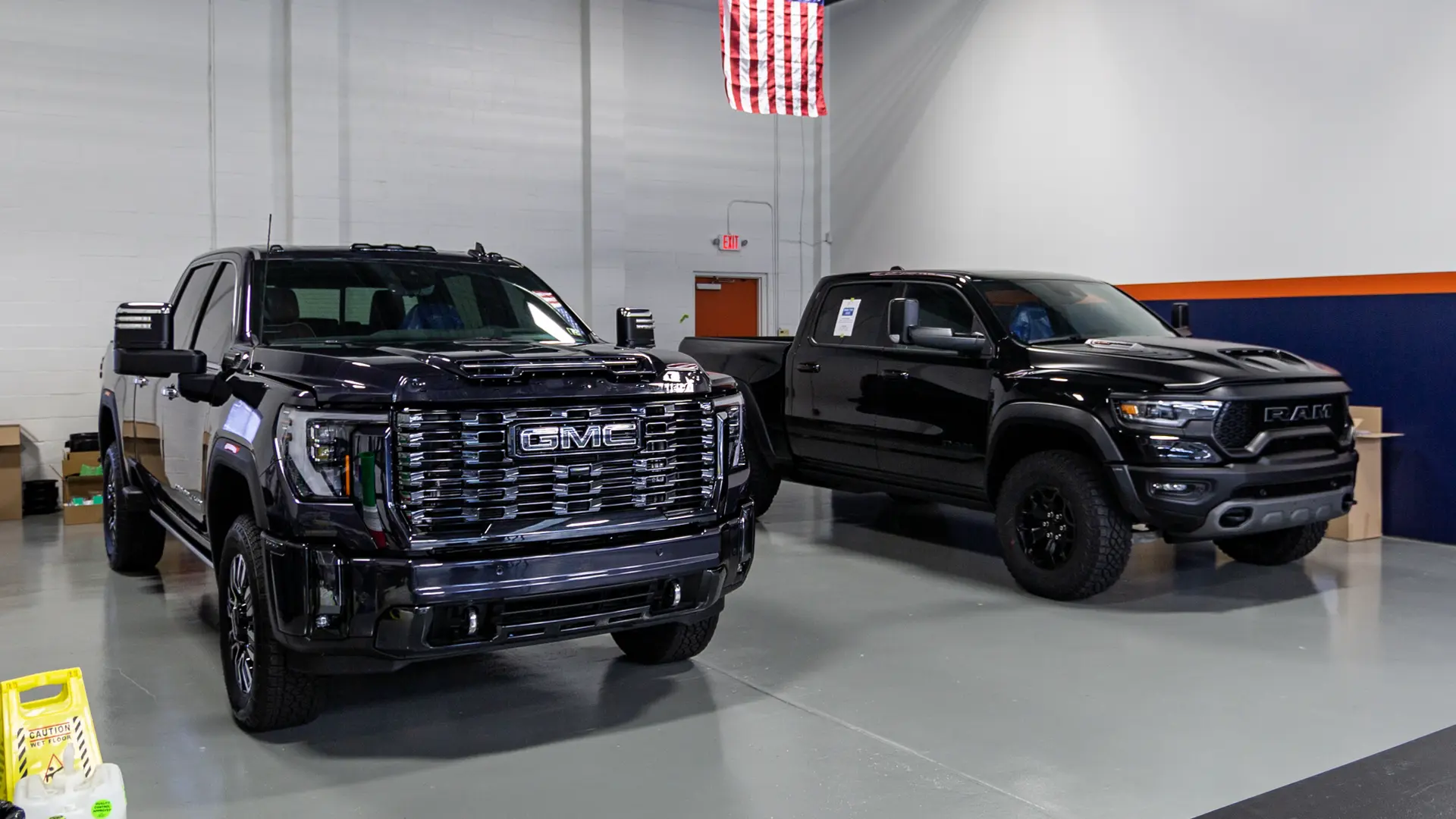 Two massive trucks, a GMC 2500 HD and a RAM TRX, sitting fully protected inside the actual Immaculate Paint Protection shop in the Lehigh Valley, both finished with SunTek PPF and Gyeon Ceramic Coating and waiting for customer pickup.