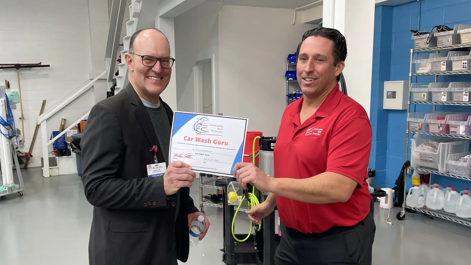 Bill Fetter of Immaculate Paint Protection sharing a laugh and presenting a "Car Wash Guru" certificate to Dr. Richard Mackenzie inside the highly organized, process-driven Lehigh Valley shop.